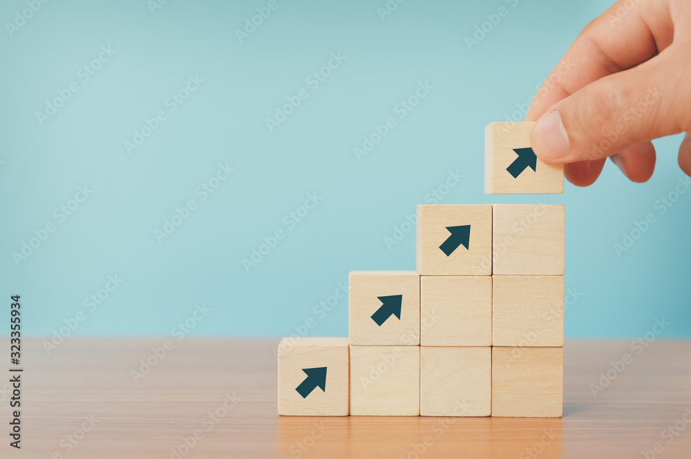 Business concept of ladder career path and growth success process. Hands of men arranging wood cube block stacking as step stair with arrow up. - obrazy, fototapety, plakaty 