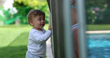 Wall Mural - Baby infant holding into swimming pool fence protection. Toddler standing outside during summer day