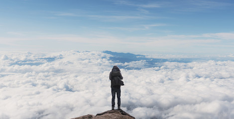 Wall Mural - a man with backpack standing on mountain top over clouds. success, achievement and outdoor adventure