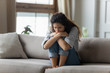 © fizkes - Stressed young woman embracing knees, sitting alone on couch.