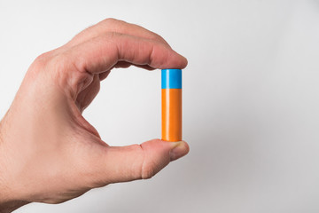 Hand holds AA alkaline battery accumulator on white background.