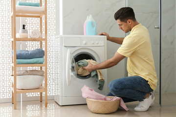 Poster - Man putting clothes into washing machine in bathroom. Laundry day