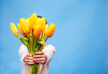 the little boy on a blue background holds in his hands a bouquet of beautiful yellow tulips. the con
