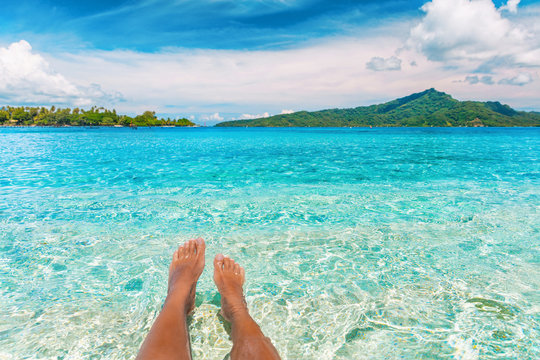 Relax feet selfie woman lying in turquoise crystalline blue water on French Polynesia motu beach vacation summer. Woman relaxing on tropical travel destination swimming sun tanning.