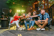 © gorynvd - Friends clinking bottles and drink beer at outdoors cozy party with music and colored disco lights.