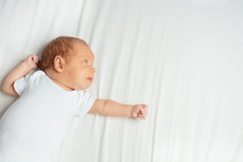 Portrait Of Newborn Infant Baby Boy Laying On The Back In The Room And Stretching Hand