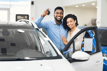 Cheerful Spouses Standing Near Car Showing Key In Dealership Center