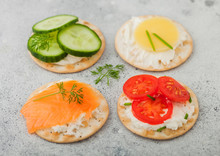 Various Round Healthy Crackers With Salmon And Cheese, Tomato And Cucumber On Light Kitchen Table Background. Top View