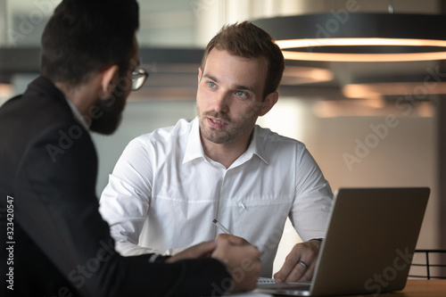 Fotografía European and arabian male colleagues talking seated at office desk
