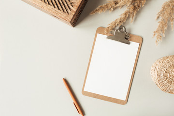Wall Mural - Flat lay minimalist home office desk with blank sheet clipboard with copy space for text, reeds branch, casket on neutral background. Top view work, business, education template.