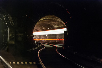 A passing train the lights of the metro tunnel.At the intersection of two metro lines.Goes into the tunnel. With red lines