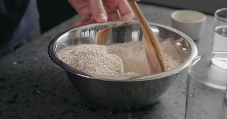 man mixing dry ingredients with flour in steel bowl on concrete countertop