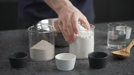 Wall Mural - man adds dry ingredients into flour in steel bowl on concrete countertop