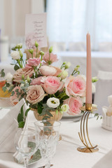 Wall Mural - A beautiful flower arrangement in a Golden vase stands on the holiday table. A Golden candlestick with a pink candle