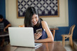 © ichzigo - Asian girl freelance using smartphone while working with her laptop in coffeeshop.