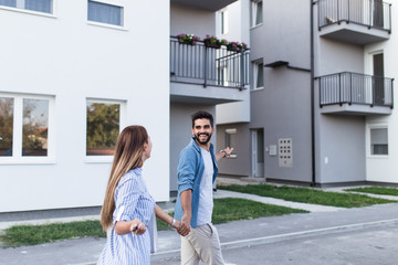 Beautiful happy young couple standing together outside in front of their new home.