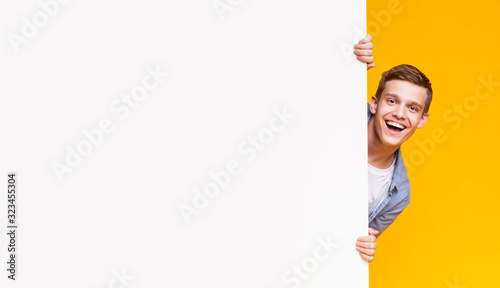 Fotografía Emotional young guy peeking out from advertising empty board