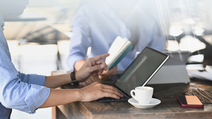 Leinwandbilder - Cropped image of smart man working as secretary typing on computer tablet and pointing his finger to notebook while sitting together with his colleague at the modern wooden table.