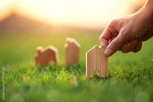 Hand of woman choosing mini wood house model on green grass, Planning buy Real Estate, eco house icon concept.