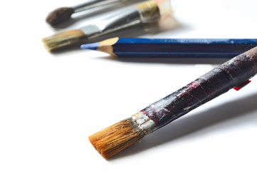 Three old paint brushes and one pencil on a white background. close-up.