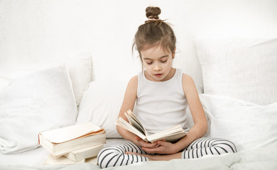 Wall Mural - Cute little girl reading a book on the bed in the bedroom.