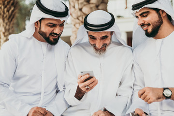 Wall Mural - Three business men walking in Dubai wearing traditional emirati clothes