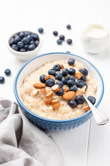 Bowl of porridge oats with blueberries, almonds on white wooden table background. Healthy breakfast, clean eating concept