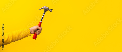 Fotomural Female hand holding hammer on yellow background, panoramic mock-up