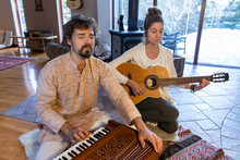Young Male And Female Meditators Meditating While Playing Harmonium And Classical Guitar As Sacred And Kirtan Music While Sitting On Floor In Room