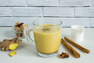 Warming tonic ginger milk tea in a glass mug with cinnamon and star anise on a white background