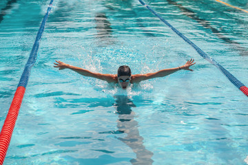 professional female swimmer swimming butterfly style in swimming pool, close up portrait