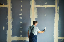Back View Portrait Of Senior Man Working On Dry Wall While Renovating House, Copy Space