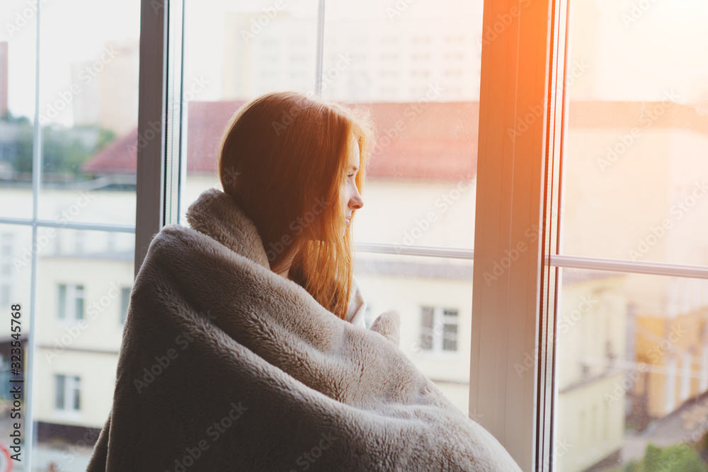thoughtful calm pensive young woman looking through the window at home wrapped in warm comfy blanket - obrazy, fototapety, plakaty 