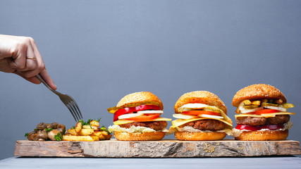 delicious rustic fast food cuisine. juicy 3 burgers potatoes and mushrooms on a gray background. eat with a fork.