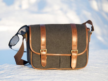 Reflective Sunglasses On A Leather And Canvas Messenger Bag On A Snow Background In The Sun