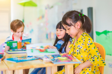 Group of Happy Children reading a book in a class of preschool. international School