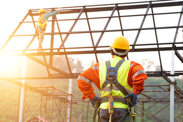 The construction worker supervises the construction of the roof structure, the construction area and the sunset background.