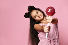 Teenage Kid With Fancy Hairstyle, In Striped Dress. She Is Holding A Huge Red Lollipop, Posing On Pink Background. Close Up