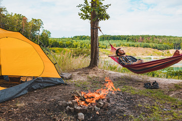 Wall Mural - man laying on hammock at lake beach near camp fire