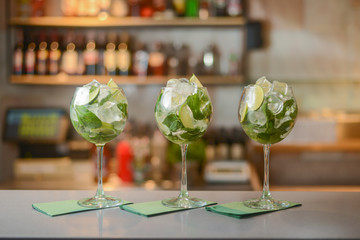 Fresh drinks Mojito with lime and ice in three clear glasses on a table in bar. Copy space.