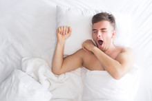 Handsome Beautiful Nice Guy, Young Sleepy Man Yawning With Open Mouth In Bed On Pillow, Covered With White Blanket, Ready For Sleep Or Just Wake Up. Healthy Good Sleeping At Home In Bedroom. Top View