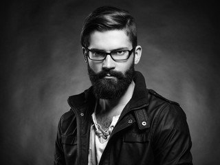 Wall Mural - Portrait of handsome man with beard and mustache. Close-up image of serious brutal bearded man on dark background. Man with glasses. Black and white photography