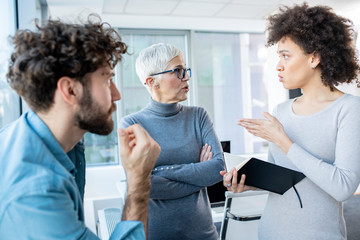 Wall Mural - A manager and two employees discussing business in an office. The female employee is holding a notebook.