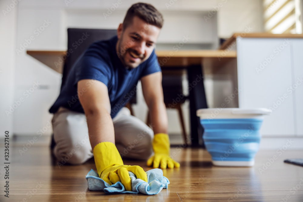 Man waxing parquet at home. Selective focus on hand with cloth. Rubber gloves on hands. Home interior. - obrazy, fototapety, plakaty 