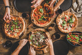 Fototapeta Na ścianę - Family or friends having pizza party dinner. Flat-lay of people taking and eating various kinds of pizza and drinking red wine over rustic wooden table, top view. Fast food lunch, celebration