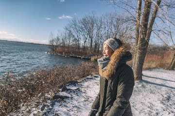 Winter cold Asian woman happy smiling in cold weather on outdoor walk sunlight in forest nature active healthy lifestyle. Young girl enjoying outside leisure walking.