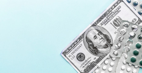 Wall Mural - pills in aluminum blister packs with one hundred dollar bill on top on a light blue background, expensive medicine flat lay with copy space