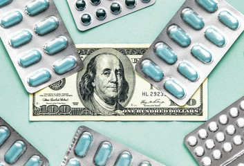 Wall Mural - money 100 dollar with white and blue pills in blister on a blue background, medicine flat lay