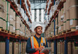 © StratfordProductions - Handsome warehouse worker uses digital tablet for checking stock, on the shelves standing cardboard boxes