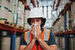 © StratfordProductions - Young warehouse manager coughing and sneezing while feeling sick and covering mouth with handkerchief standing in factory